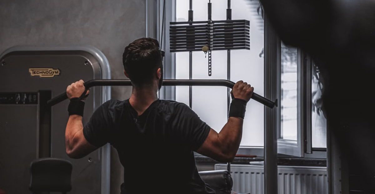 Back view of a man exercising with lat pulldown machine in the gym.